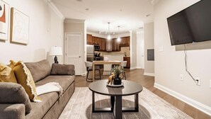 A living room with a sofa, coffee table, and artwork on the wall. - Landing | Modern 1BD, Courtyard, Gym (Cary)