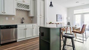 Et moderne køkken med hvide skabe, en rustfri opvaskemaskine, indbygget ovn og en bar med barstole.