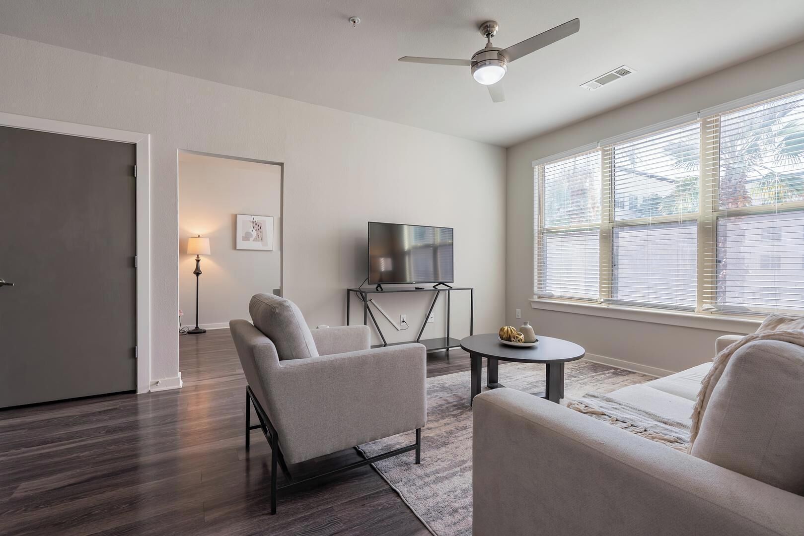 A modern living room with a flat-screen TV, two armchairs, a coffee table, and a ceiling fan.
