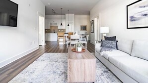 A modern living room with a sofa, coffee table, and a TV mounted on the wall. - Landing | Modern 2BD, Pool, Rooftop Lounge (Cary)