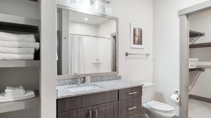 A modern bathroom with a granite countertop, a large mirror, a shower, and a toilet. - Landing | Modern 2BD, Clubhouse, Gym (McKinney)