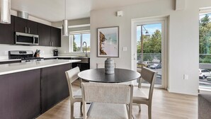 A modern kitchen with dark cabinets, a central island, and a dining area with two chairs and a table. - Landing | Amazing 2BD, Gym, Pool (Portland)