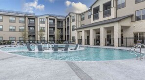 Ein modernes Apartmenthaus mit einem zentral gelegenen Schwimmbecken, umgeben von Liegestühlen.