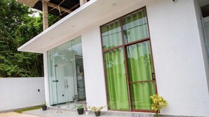 Un bâtiment moderne avec une entrée en verre, un rideau vert devant une fenêtre et des plantes en pot sur les marches.