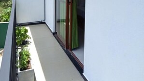 Un balcon étroit avec une porte vitrée et un rideau vert.