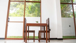 Une pièce avec une table et des chaises en bois, de grandes fenêtres donnant sur un paysage verdoyant et un sol carrelé.