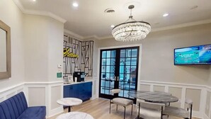 Un salon moderne avec un canapé bleu, une table basse ronde, une table à manger avec des chaises, un lustre et un téléviseur fixé au mur.