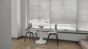 A corner room with a white round table and two chairs, a large window with blinds, and a carpeted floor. - Landing | Spectacular 1BD, Gym (Birmingham)