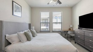 A neatly arranged bedroom with a bed, a desk, a chair, and a television.