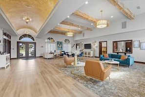 A spacious living area with a high ceiling, wooden beams, and a large window.