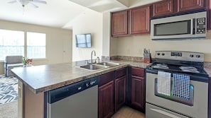 A kitchen with a dishwasher, double sink, microwave, stove, and wooden cabinets.