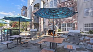Une terrasse extérieure avec des tables et des bancs en pierre, une cheminée en pierre et un barbecue.