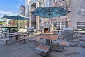 Eine Terrassengaststätte mit Steintischen und -bänken, einem Kamin aus Stein und einem Grill.