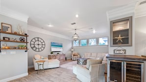 A spacious living room with a large clock, a chandelier, and a family-themed wall decor.