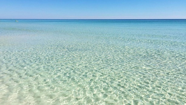 A clear view of a beach with shallow, clear water and a distant horizon.