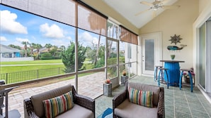 A covered patio with wicker furniture, a ceiling fan, and a view of a green lawn and houses.