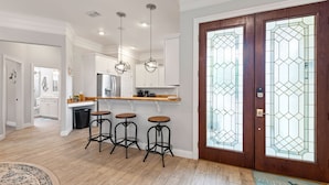 A modern kitchen with white cabinets, a wooden countertop, and three bar stools.