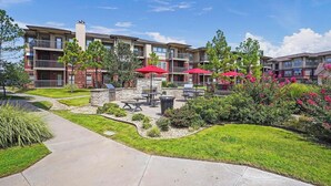 A residential building with a patio area featuring outdoor seating and barbecue grills. - Landing | Modern 2BD, Pool, Gym (Jenks)