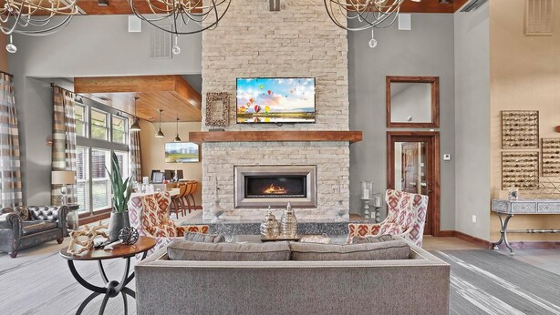A spacious living room with a stone fireplace, comfortable seating, and a large TV mounted above it. - Landing | Modern 2BD, Pool, Gym (Jenks)