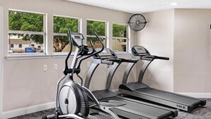 Et fitnessrum med løbebånd, crosstrainer og motionscykel, med vinduer der giver udsigt ud.