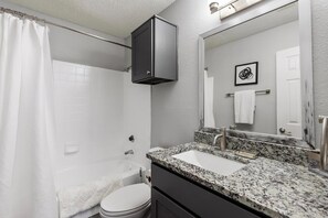 A bathroom with a shower, toilet, sink, and a cabinet above the mirror. - Landing | Beautiful 1BD, Gym, Courtyard (Grand Prairie)