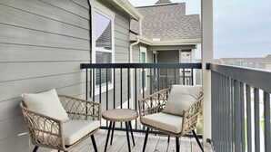 A balcony with two wicker chairs and a small round table, overlooking a residential area. - Landing | Stunning 1BD, Clubhouse, Gym (Belton)