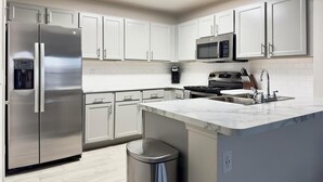 A modern kitchen with white cabinets, stainless steel appliances, a marble countertop, and a built-in trash can. - Landing | Stunning 1BD, Clubhouse, Gym (Belton)