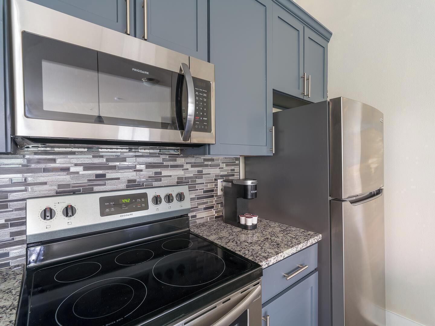 A kitchen with a stainless steel microwave, a built-in oven, a refrigerator, and granite countertops.