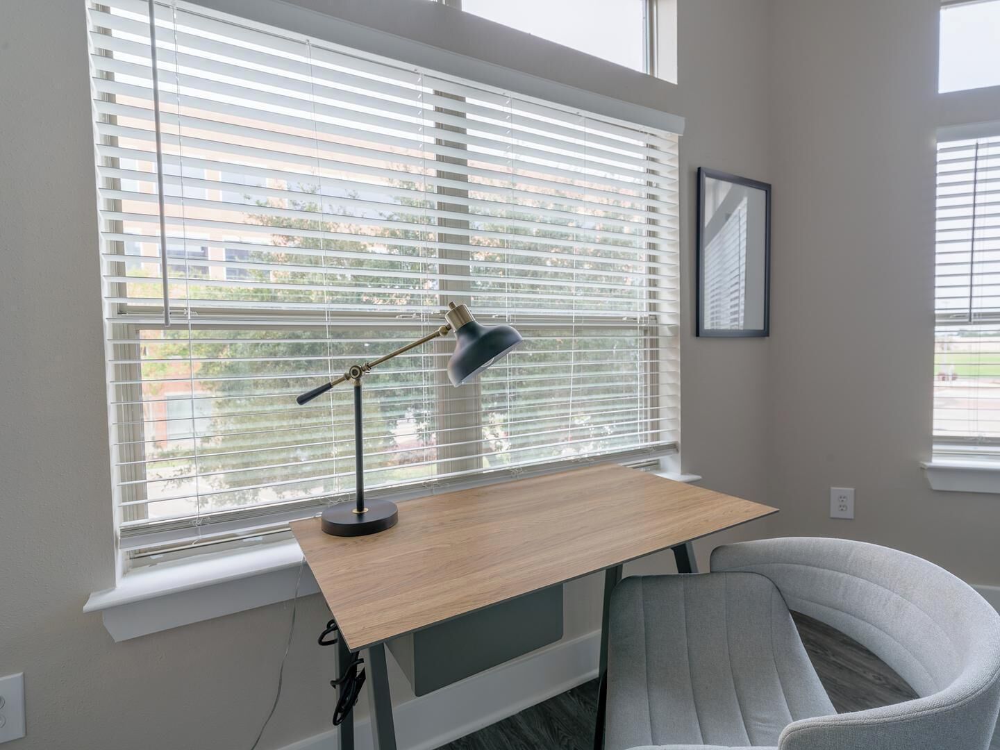 Une chambre moderne équipée d’un bureau, d’une chaise et de grandes fenêtres avec stores.