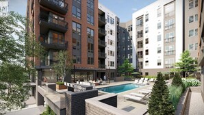 A modern apartment building with a rooftop pool area, outdoor seating, and a mix of brick and white facades.