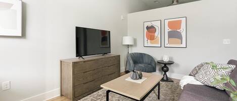 A modern living room with a flat-screen TV on a wooden cabinet, a grey sofa, a coffee table, and abstract art on the wall.