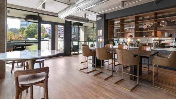 Ein moderner Essbereich mit rundem Tisch und Stühlen, eine Küche mit offenen Regalen und große Fenster mit Blick auf die Stadt.