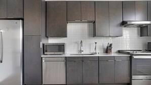 A modern kitchen with dark cabinetry, a stainless steel refrigerator, a microwave, and a sink with a faucet.