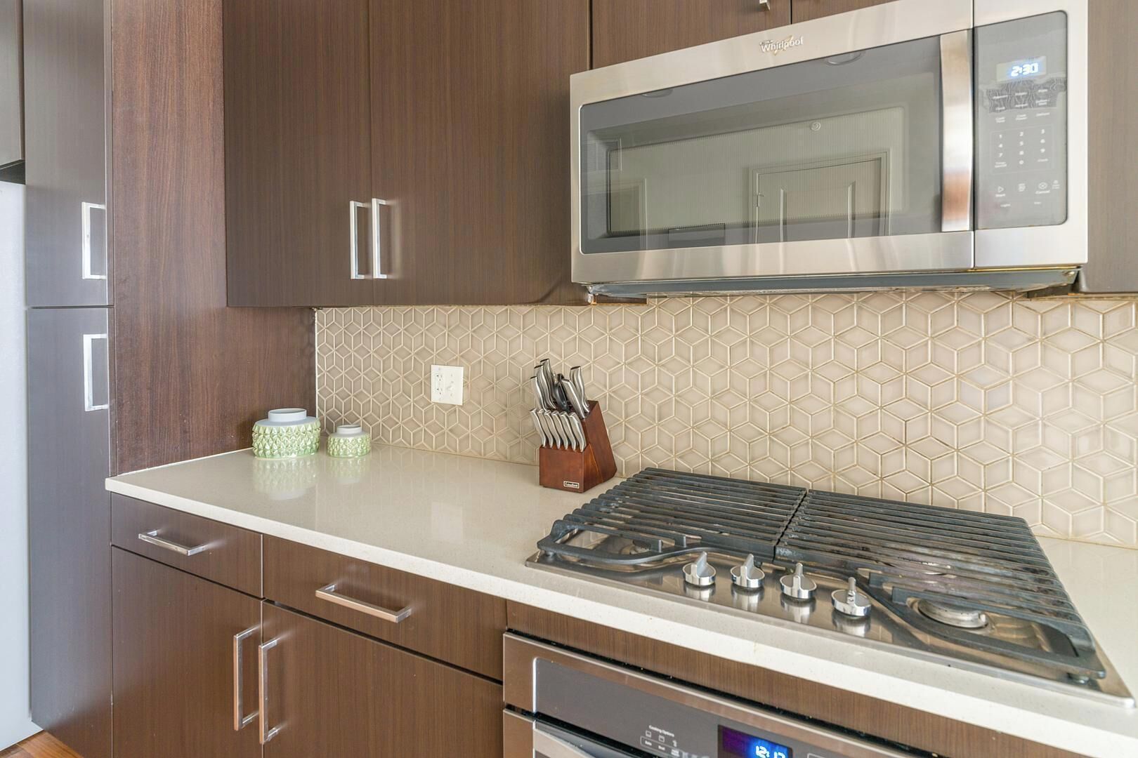 A kitchen with a stainless steel microwave, a gas stove, and wooden cabinets.