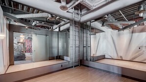 Quarto moderno em estilo industrial, com dutos aparentes, escada e um espelho grande refletindo o interior do aposento.
