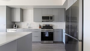 Uma cozinha moderna com armários cinzas, uma geladeira de aço inoxidável, micro-ondas e forno.