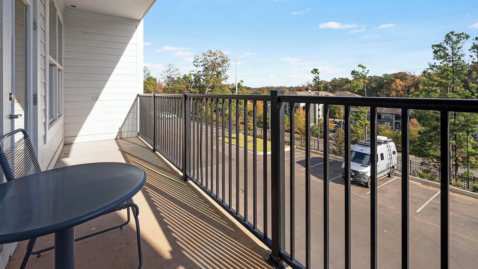 A balcony with a table and chairs, overlooking a parking area and trees.