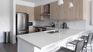 A modern kitchen with stainless steel appliances, a large island with bar stools, and wooden cabinetry. - Landing | Incredible 2BD, Clubhouse, Pool (Birmingham)