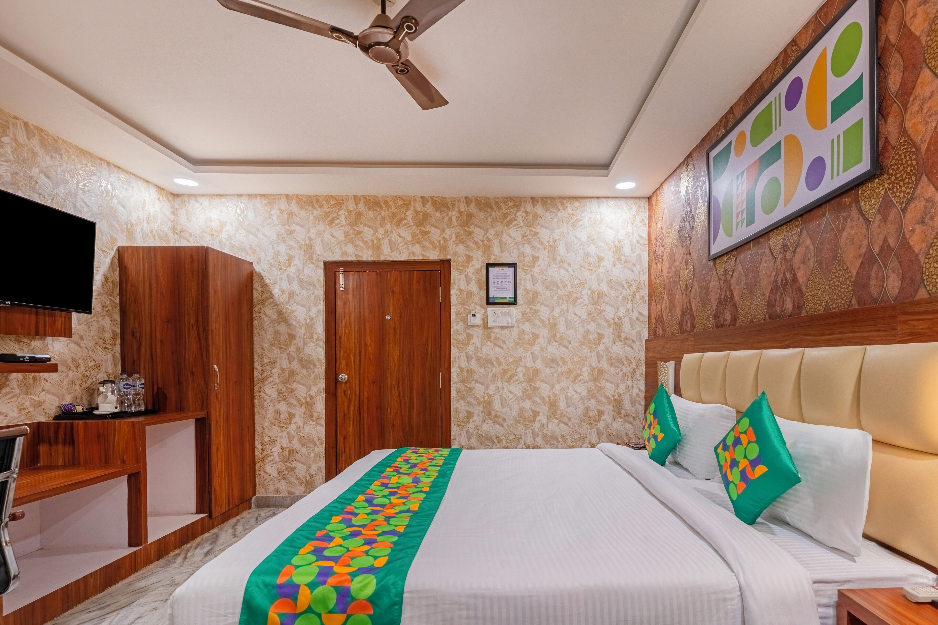 Une chambre d’hôtel équipée d’un lit, d’une télévision, d’une armoire en bois et d’un ventilateur de plafond.