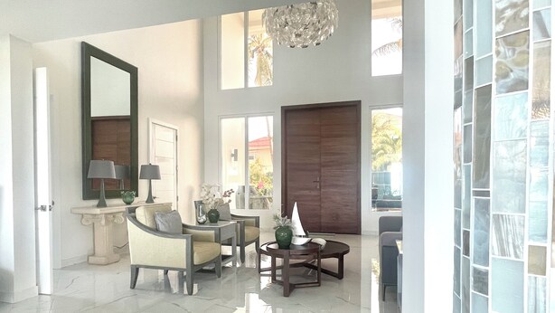A spacious living room with a marble floor, a large chandelier, and a view of the outdoors through large windows.