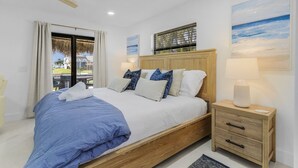 Un dormitorio con cama, mesita de noche, ventilador de techo, ventana con cortinas y obras de arte en las paredes.