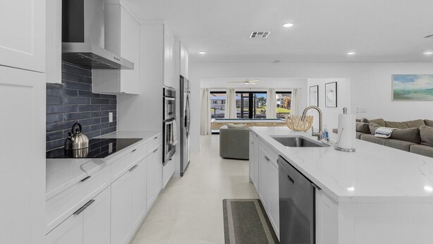Una cocina moderna con armarios blancos, un salpicadero de azulejos negros y electrodomésticos de acero inoxidable.