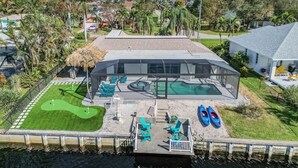 Una casa moderna con piscina, un patio cubierto y un pequeño muelle para barcos.