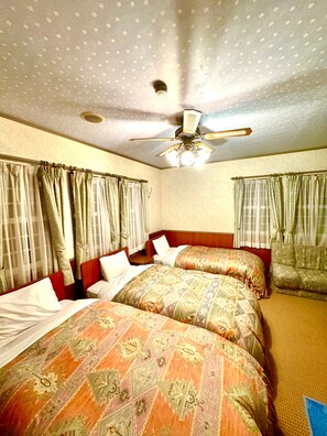 Une chambre d’hôtel avec deux lits, un ventilateur de plafond et des rideaux.