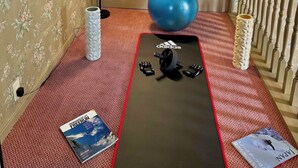 Una habitación con una puerta, una pelota de ejercicios azul, un tapete negro con la marca Adidas y dos libros en el suelo.
