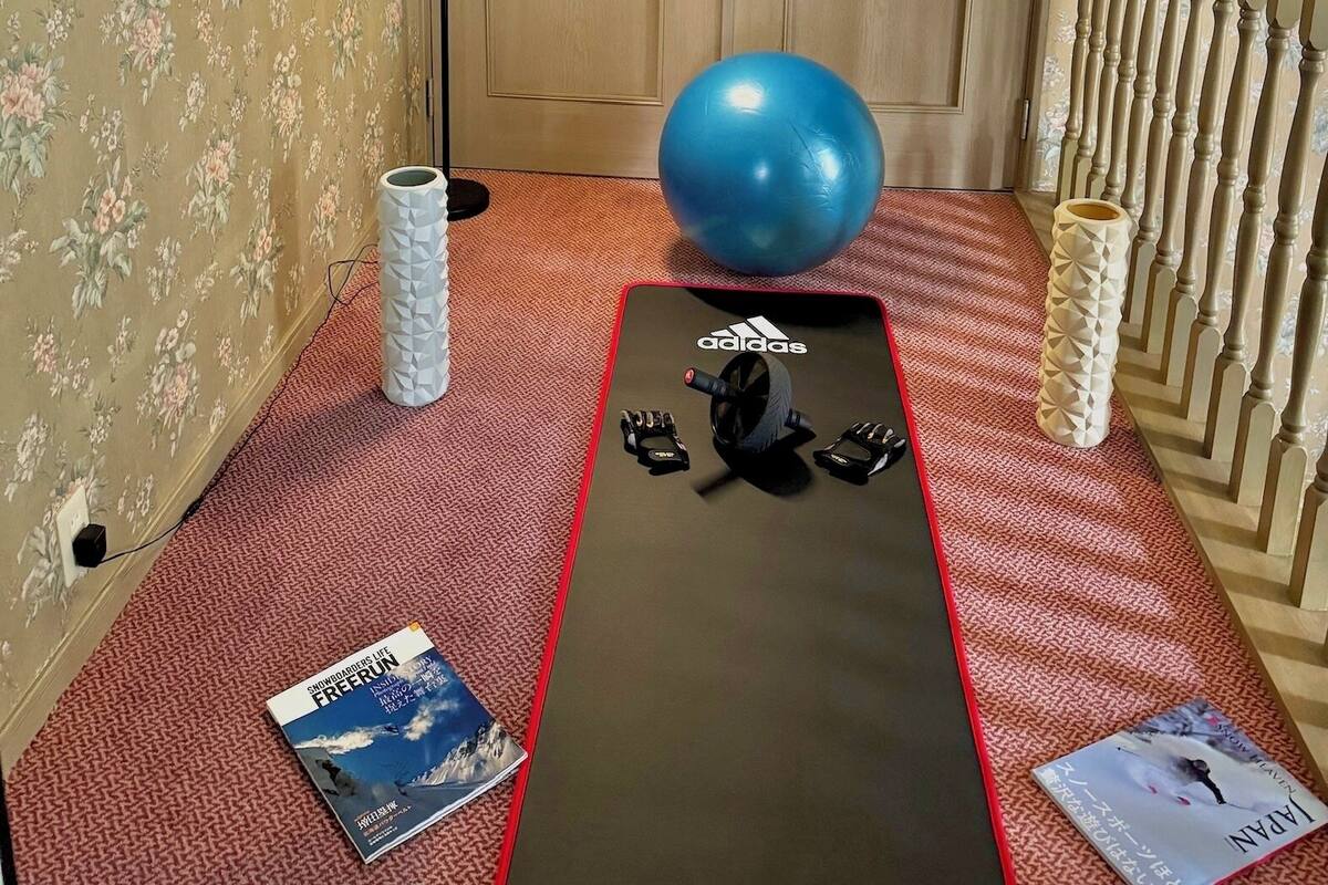 A room with a door, a blue exercise ball, a black mat with Adidas branding, and two books on the floor.
