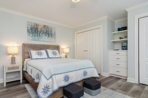 A bedroom with a bed, bedside lamps, a nightstand, a wooden headboard, a wall-mounted artwork, a wardrobe, and a built-in shelving unit.