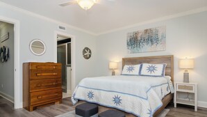 Une chambre à coucher avec une commode en bois, un lit recouvert d’une couvre-lit à motifs d’étoiles, deux lampes de chevet et un ventilateur de plafond.