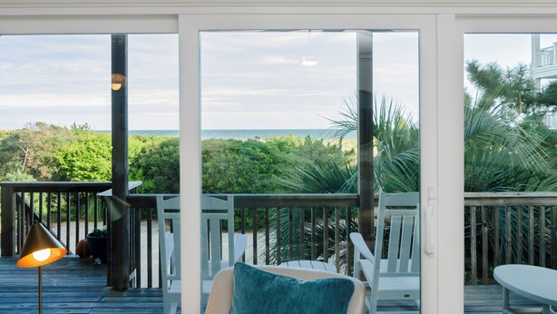 Un balcon avec vue sur l’océan, des balustrades en bois et un pot de fleurs.