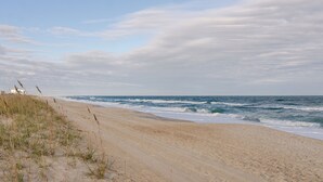Une plage de sable avec des vagues, une jetée en arrière-plan et un ciel nuageux.
